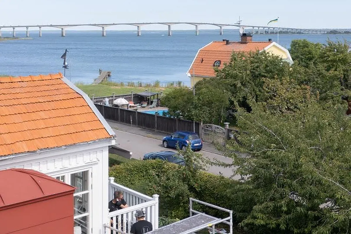 Målare på byggställningen vid en vit villa med orange tegeltak, Kalmarsund och Ölandsbron i bakgrunden