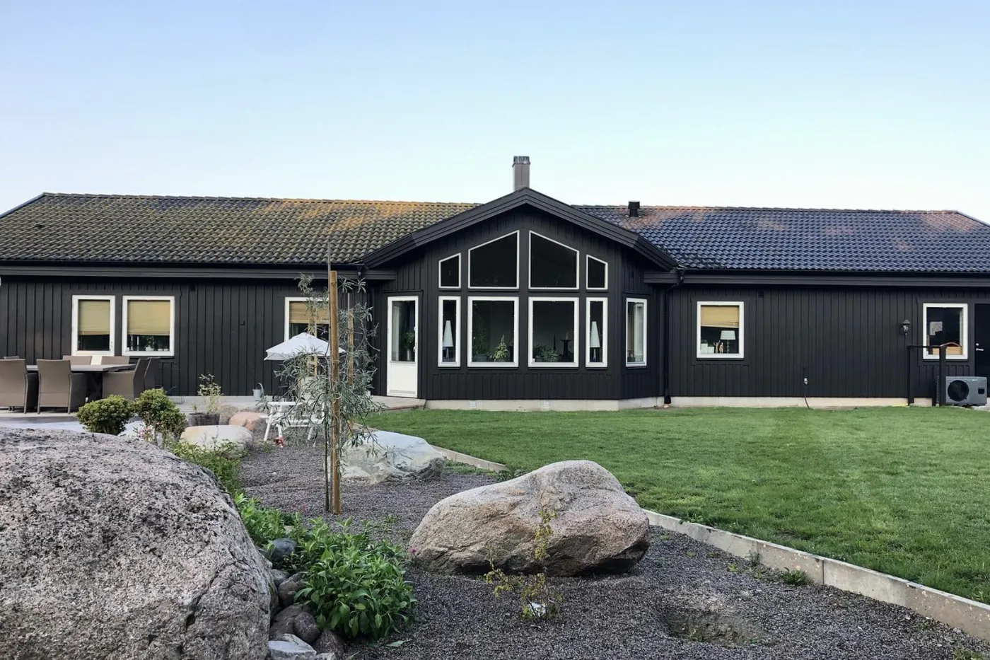 Mörk trävilla med vita fönster och stor glasad gavel, med trädgård och stenblock framför